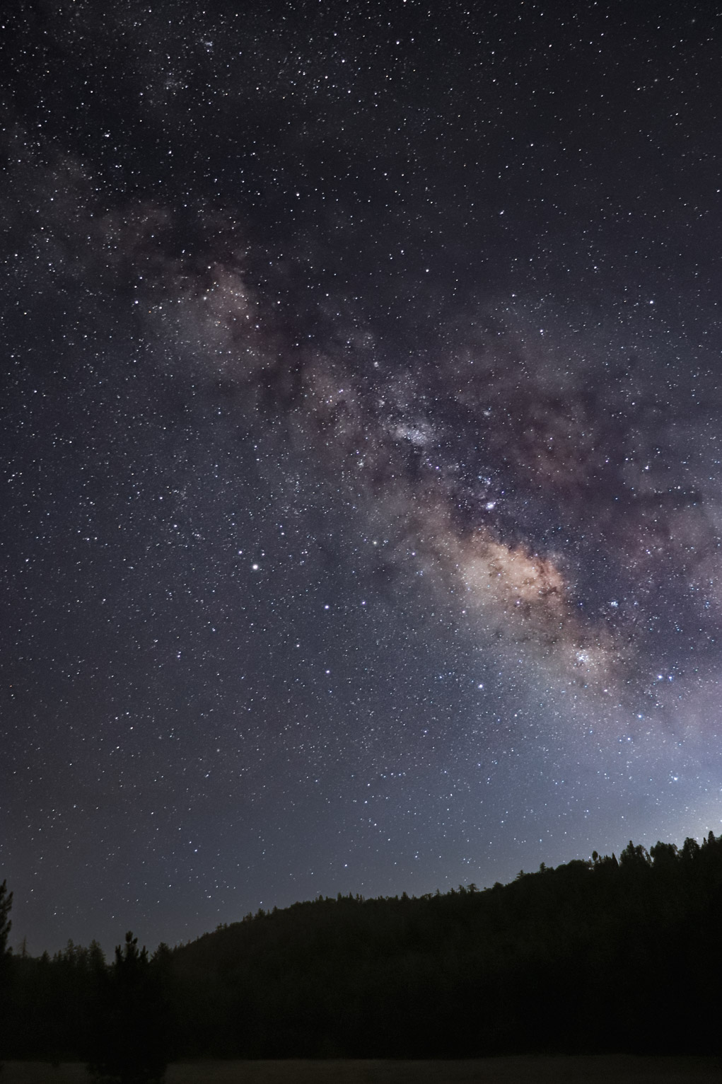 the milky way rises bright over a hill